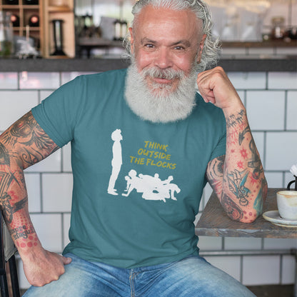 An older man with a white beard and tattoos sits in a cafe setting wearing a teal t-shirt with a white graphic of a person and the text 'THINK OUTSIDE THE FLOCKS'.