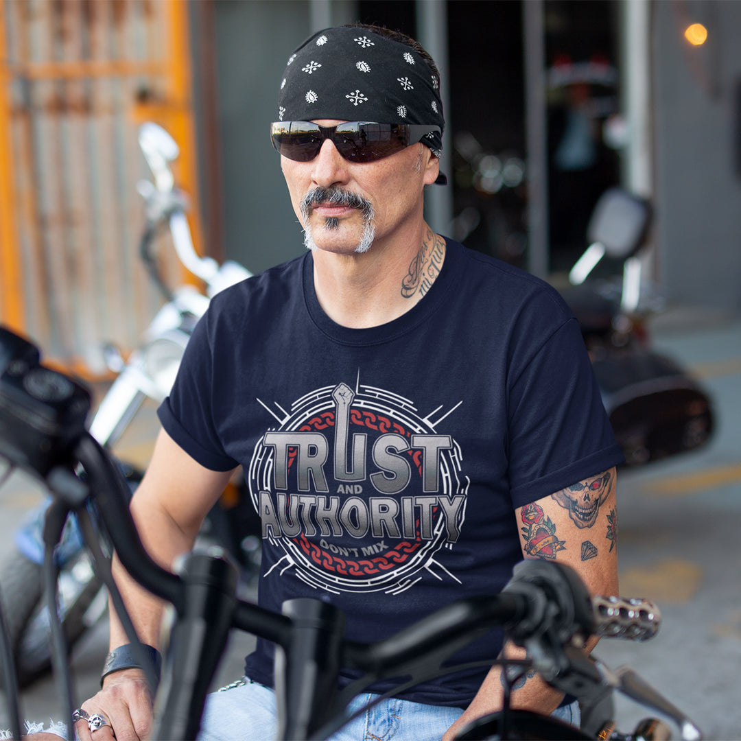 Man wearing a black bandana and sunglasses, sitting on a motorcycle with a 'Trust and Authority' t-shirt. A broken society t shirt design with trust issues. At first glance this street art design gives the impression of trust for authority, but with a closer look it suggests there is no connection between the two. Made from 100% organic ring-spun cotton, this demo t shirt design is unisex, high quality, super comfy, and best of all, eco-friendly.