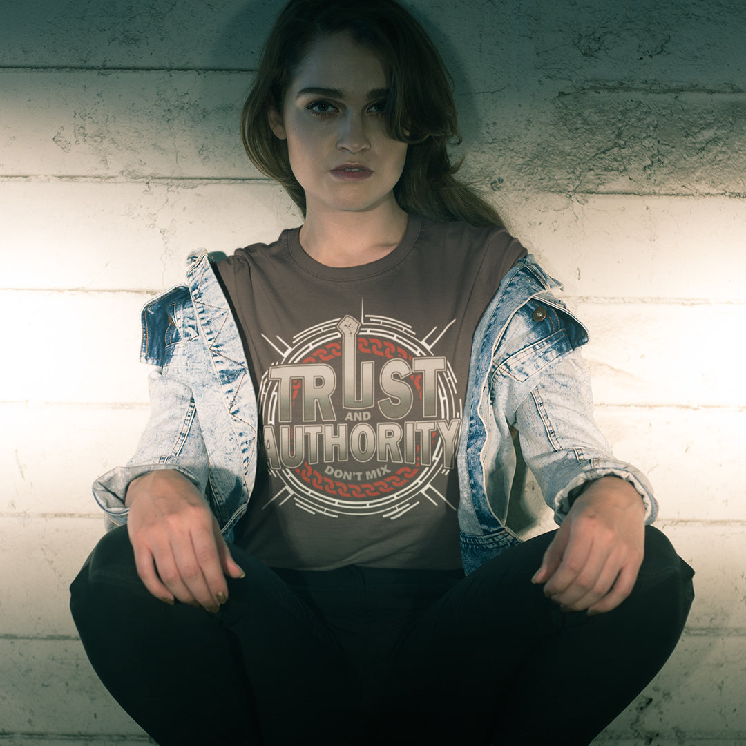 Person wearing a shirt with 'Trust and Authority' text against a textured wall. A broken society t shirt design with trust issues. At first glance this street art design gives the impression of trust for authority, but with a closer look it suggests there is no connection between the two. Made from 100% organic ring-spun cotton, this demo t shirt design is unisex, high quality, super comfy, and best of all, eco-friendly.