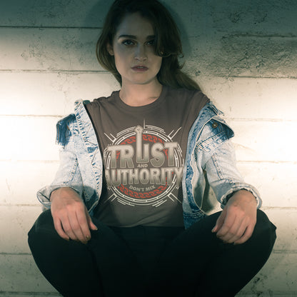 Person wearing a shirt with 'Trust and Authority' text against a textured wall. A broken society t shirt design with trust issues. At first glance this street art design gives the impression of trust for authority, but with a closer look it suggests there is no connection between the two. Made from 100% organic ring-spun cotton, this demo t shirt design is unisex, high quality, super comfy, and best of all, eco-friendly.