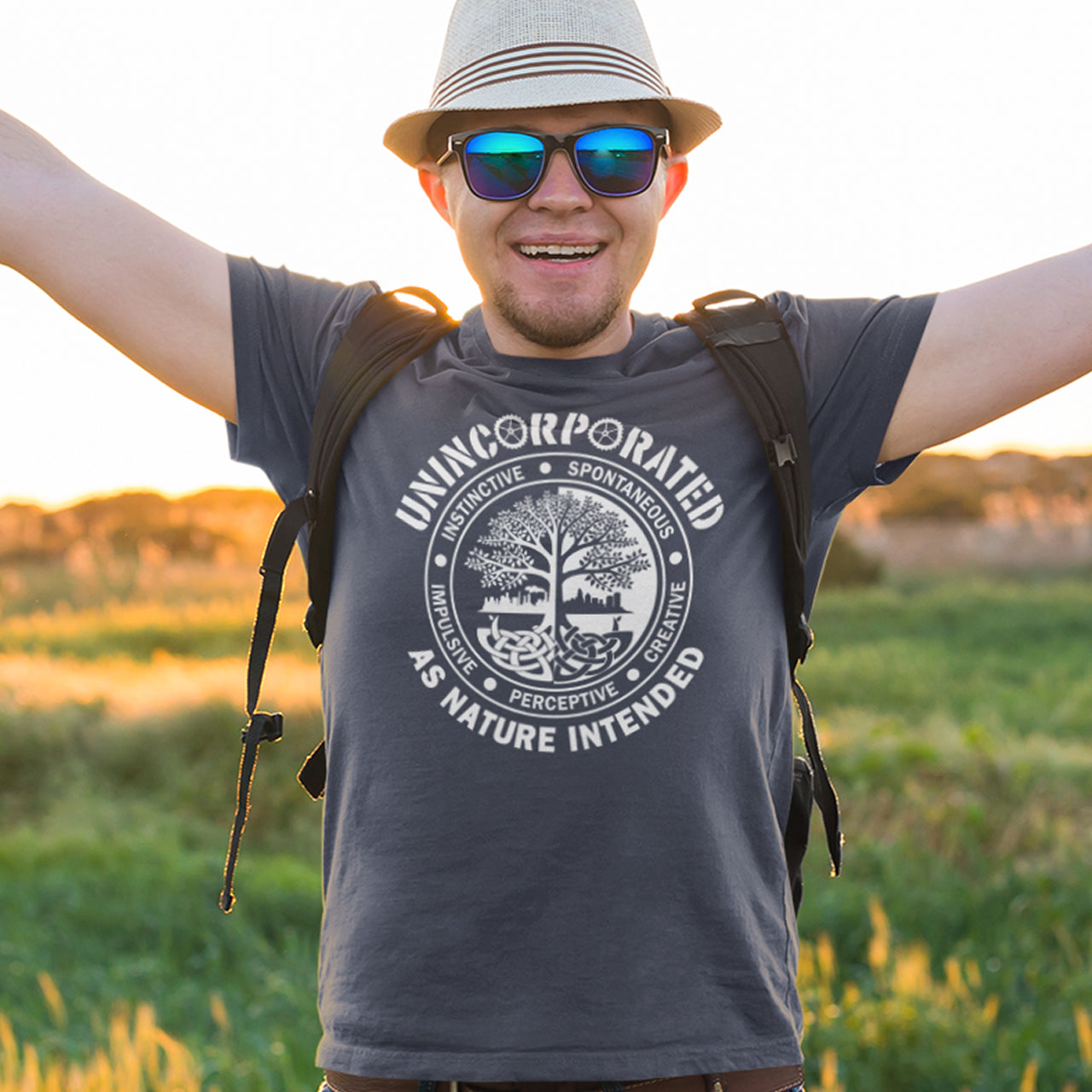 Man standing in the countryside wearing an anthracite t shirt with 'unincorporated' text. This anti corporate t shirt defines corporations as unnatural and indoctrinating. A design for people who are proud to be a human animal and not programmed into the corporate machine. Urban art using the tree of life as a centre piece. Made from 100% organic ring-spun cotton, this non conformist t shirt is unisex, high-quality, super comfy, and best of all—eco-friendly.