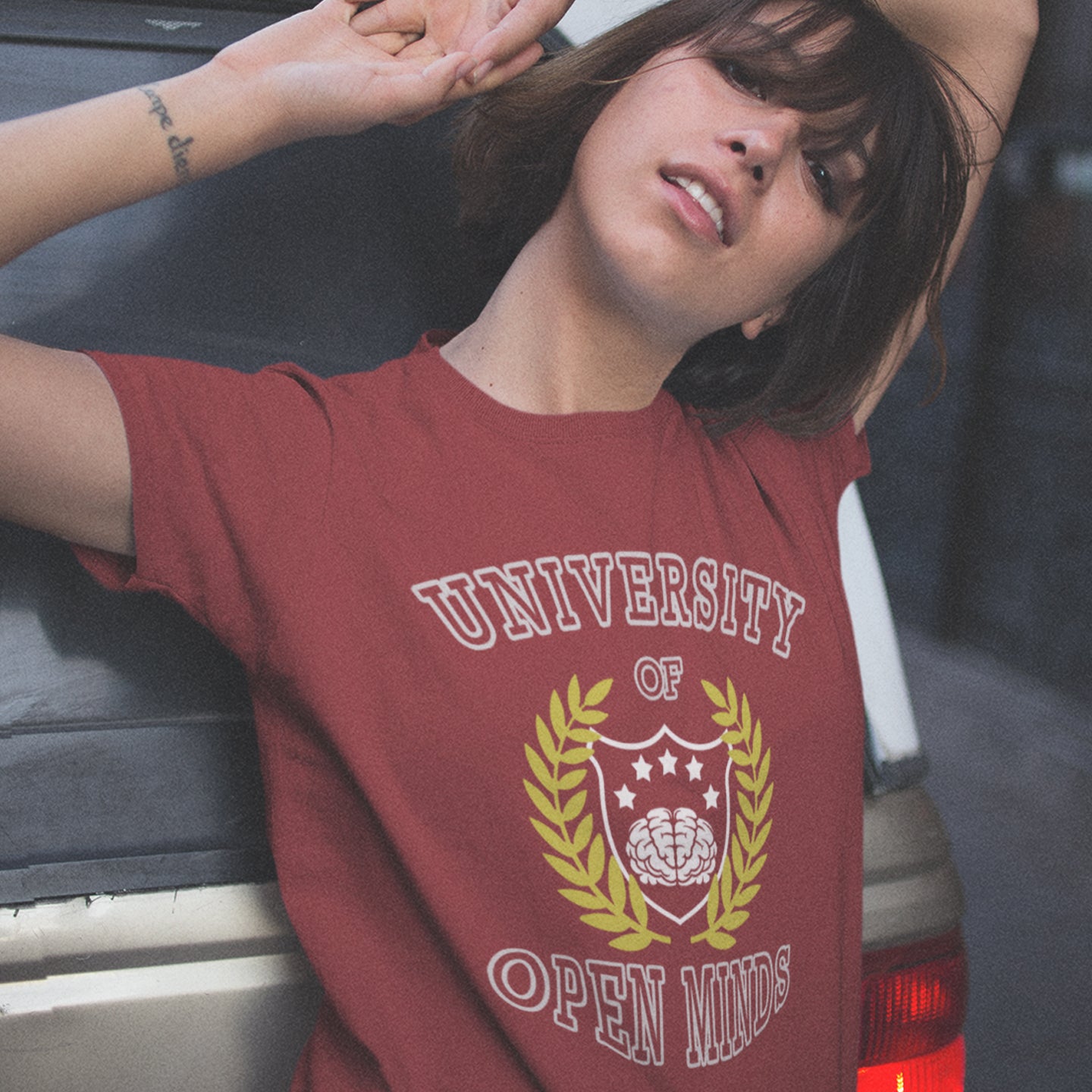 Person wearing a red t-shirt with 'University of Open Minds' design, leaning against a vehicle. A cool graphic design for the liberal minded. If you think outside the box then this university is for you. Only practical lessons and no student loan required. Made from 100% organic ring-spun cotton, this social awareness t-shirt is unisex, high-quality, super comfy, and best of all, eco-friendly.