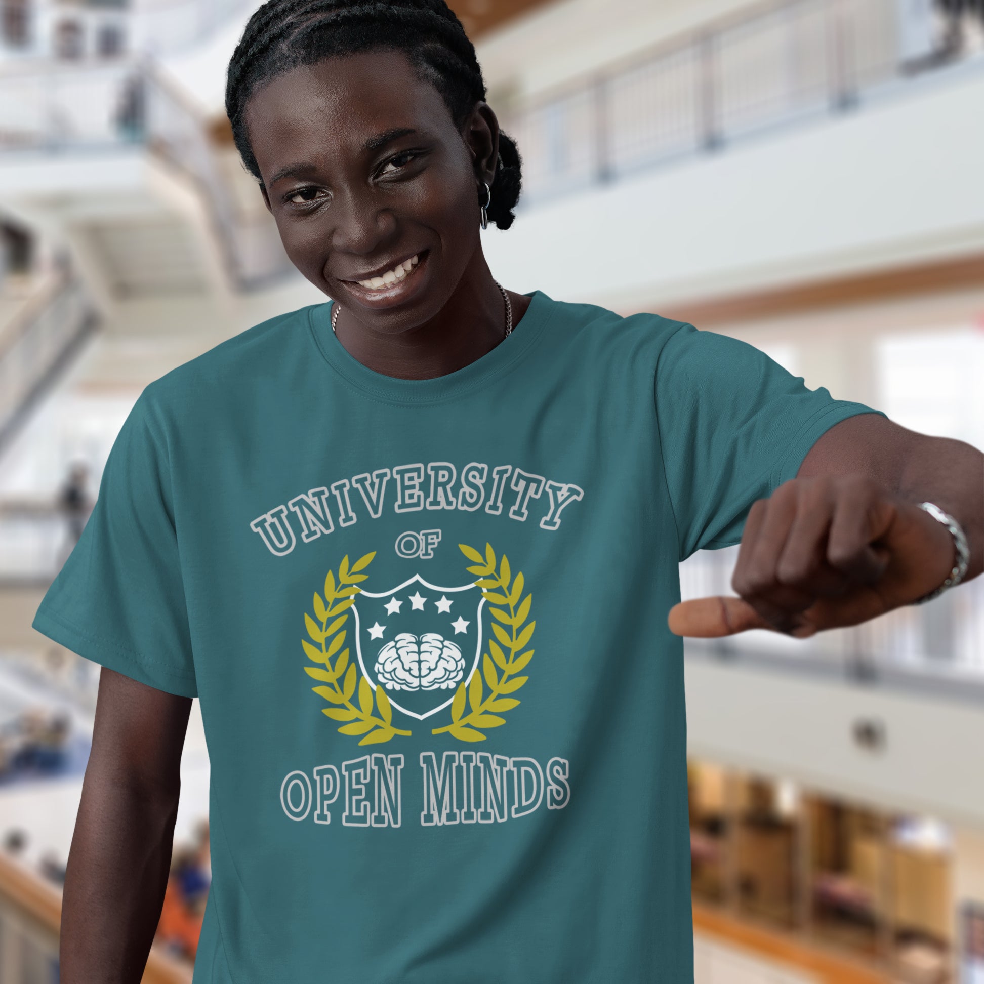 Person wearing a teal t-shirt with 'University of Open Minds' design in an indoor setting. A cool graphic design for the liberal minded. If you think outside the box then this university is for you. Only practical lessons and no student loan required. Made from 100% organic ring-spun cotton, this social awareness t-shirt is unisex, high-quality, super comfy, and best of all, eco-friendly.
