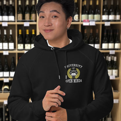 Person wearing a black hoodie with a logo and text in a wine store. A graphic hoodie design for the liberal minded. If you think outside the box then this university is for you. Only practical lessons and no student loan required. Comfortable and practical. It's extra soft and has a convenient front pouch pocket. Made from organic cotton and recycled polyester, this graphic hoodie is a great eco-friendly choice.