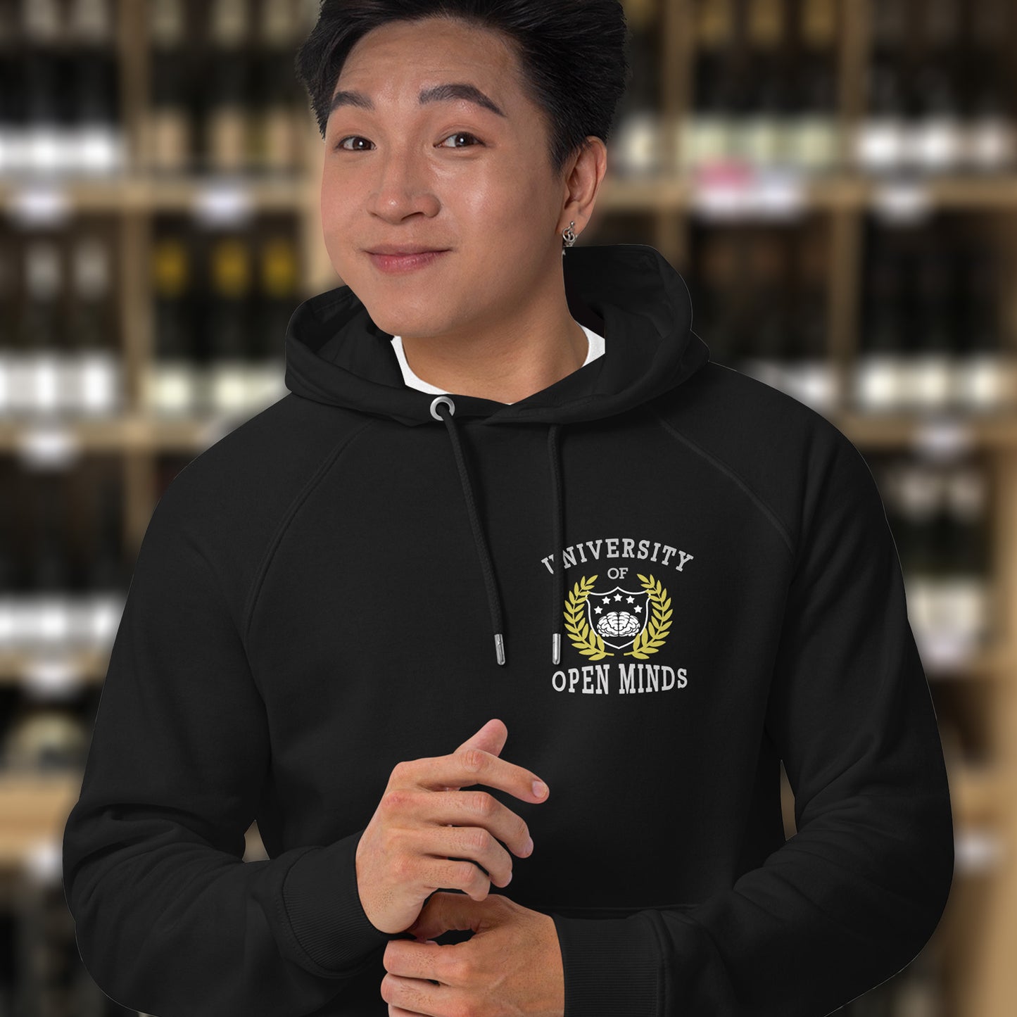 Person wearing a black hoodie with a logo and text in an indoor setting. A fake university hoodie design for the liberal minded. If you think outside the box then this university is for you. Only practical lessons and no student loan required. Comfortable and practical. It's extra soft and has a convenient front pouch pocket. Made from organic cotton and recycled polyester, this non conformist hoodie is a great eco-friendly choice.