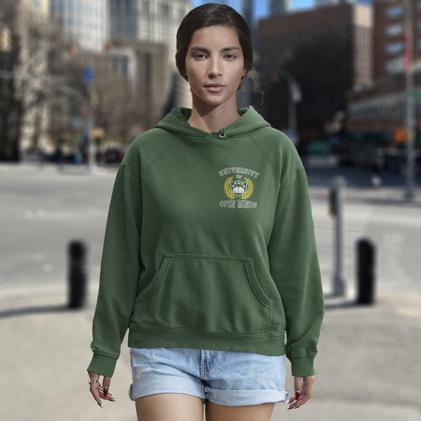 Woman wearing a khaki hoodie with a logo on a city street. A fake university hoodie design for the liberal minded. If you think outside the box then this university is for you. Only practical lessons and no student loan required. Comfortable and practical. It's extra soft and has a convenient front pouch pocket. Made from organic cotton and recycled polyester, this non conformist hoodie is a great eco-friendly choice.