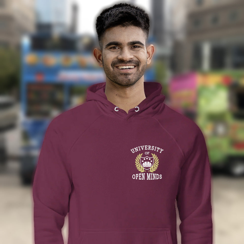 Man wearing a burgundy hoodie with 'University of Open Minds' logo, blurred background. A fake university hoodie design for the liberal minded. If you think outside the box then this university is for you. Only practical lessons and no student loan required. Comfortable and practical. It's extra soft and has a convenient front pouch pocket. Made from organic cotton and recycled polyester, this non conformist hoodie is a great eco-friendly choice.