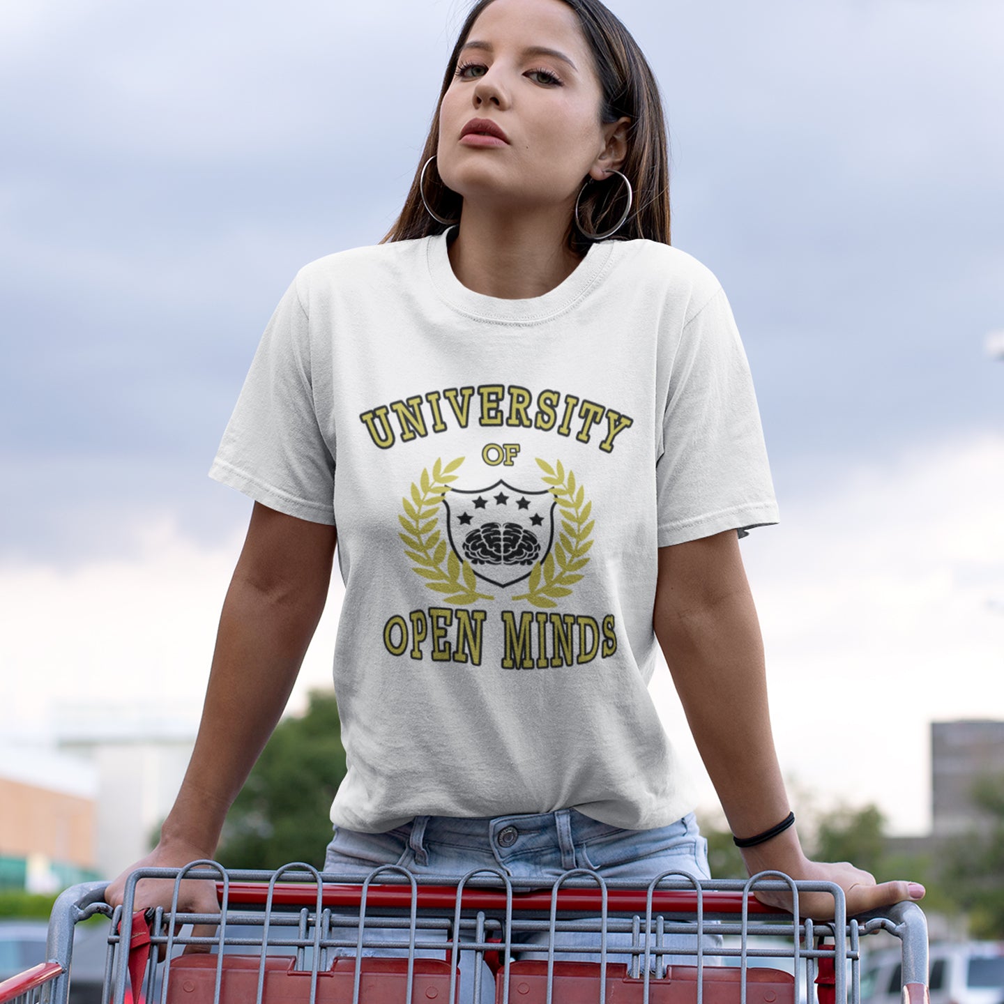 Person wearing a white t-shirt with 'University of Open Minds' design, standing outdoors. A cool graphic design for the liberal minded. If you think outside the box then this university is for you. Only practical lessons and no student loan required. Made from 100% organic ring-spun cotton, this social awareness t-shirt is unisex, high-quality, super comfy, and best of all, eco-friendly.