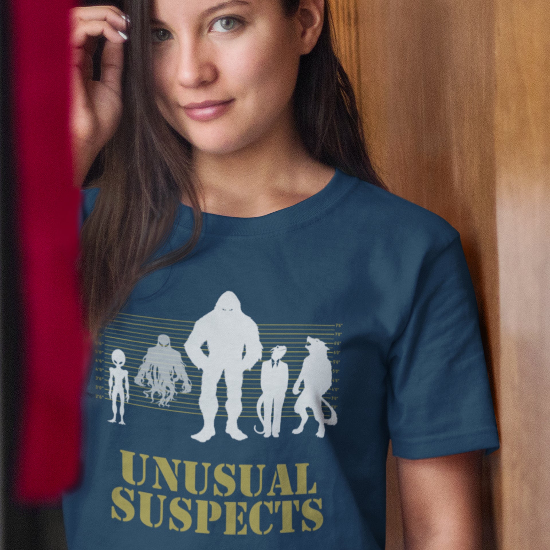 Woman wearing a blue t-shirt with 'Unusual Suspects' graphic design. A design for movie loving conspiracy theorists. From bigfoot to aliens, these are the personnel responsible for most cover ups and disputed existence. This imaginative stencil art is truly for people who think outside the box. Made from 100% organic ring-spun cotton, this witty conspiracy theory t-shirt is unisex, high-quality, super comfy, and best of all, eco-friendly.