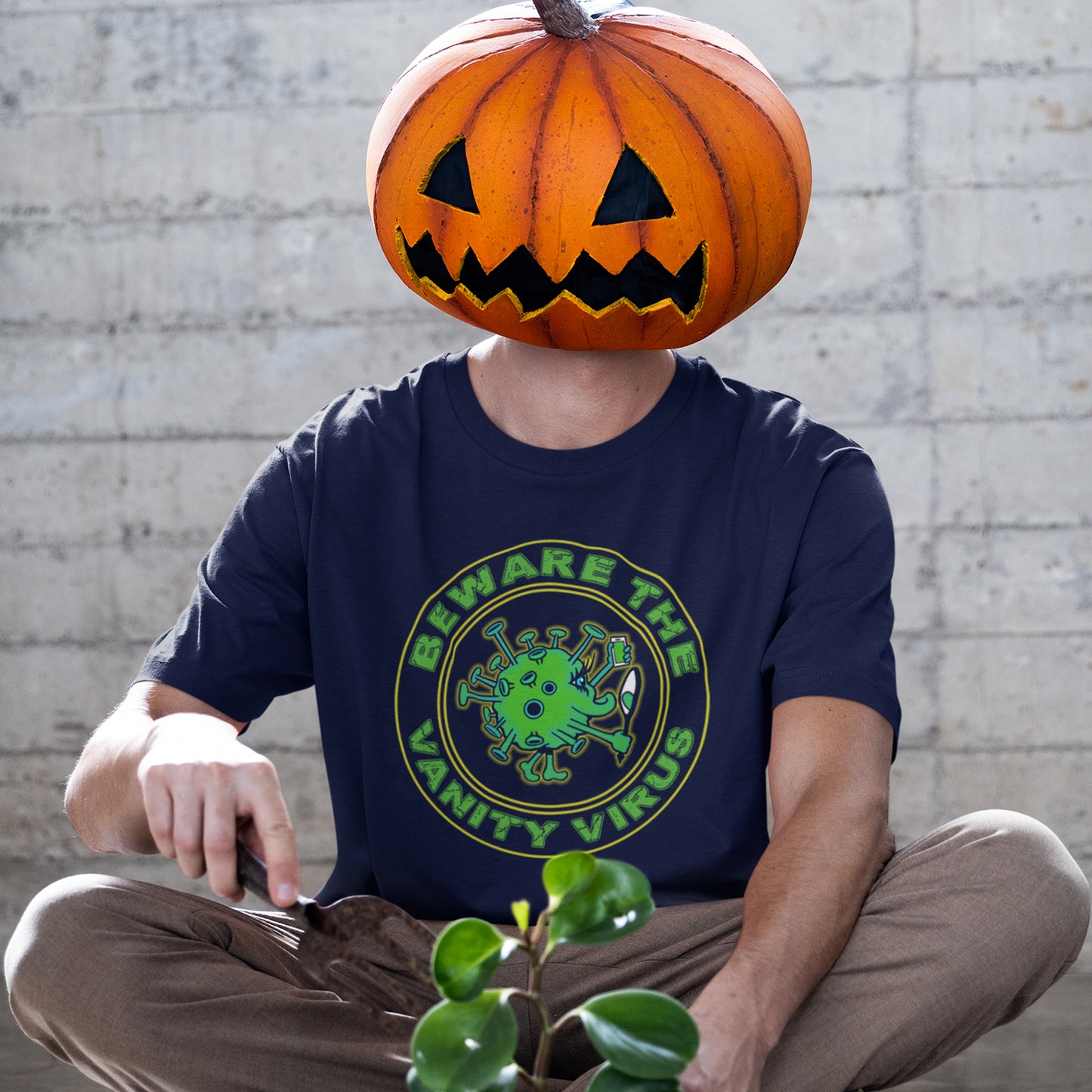Person wearing a French navy blue t-shirt with a Halloween-themed design, sitting against a brick wall. This satirical counterculture t-shirt suggest there are some nasty viruses out there and vanity is one of the oldest. This unique t-shirt design promotes social awareness of the dangers of vanity because it's a bitch once it takes hold. Made from 100% organic ring-spun cotton, this witty counterculture t-shirt is unisex, high-quality, super comfy, and best of all, eco-friendly.