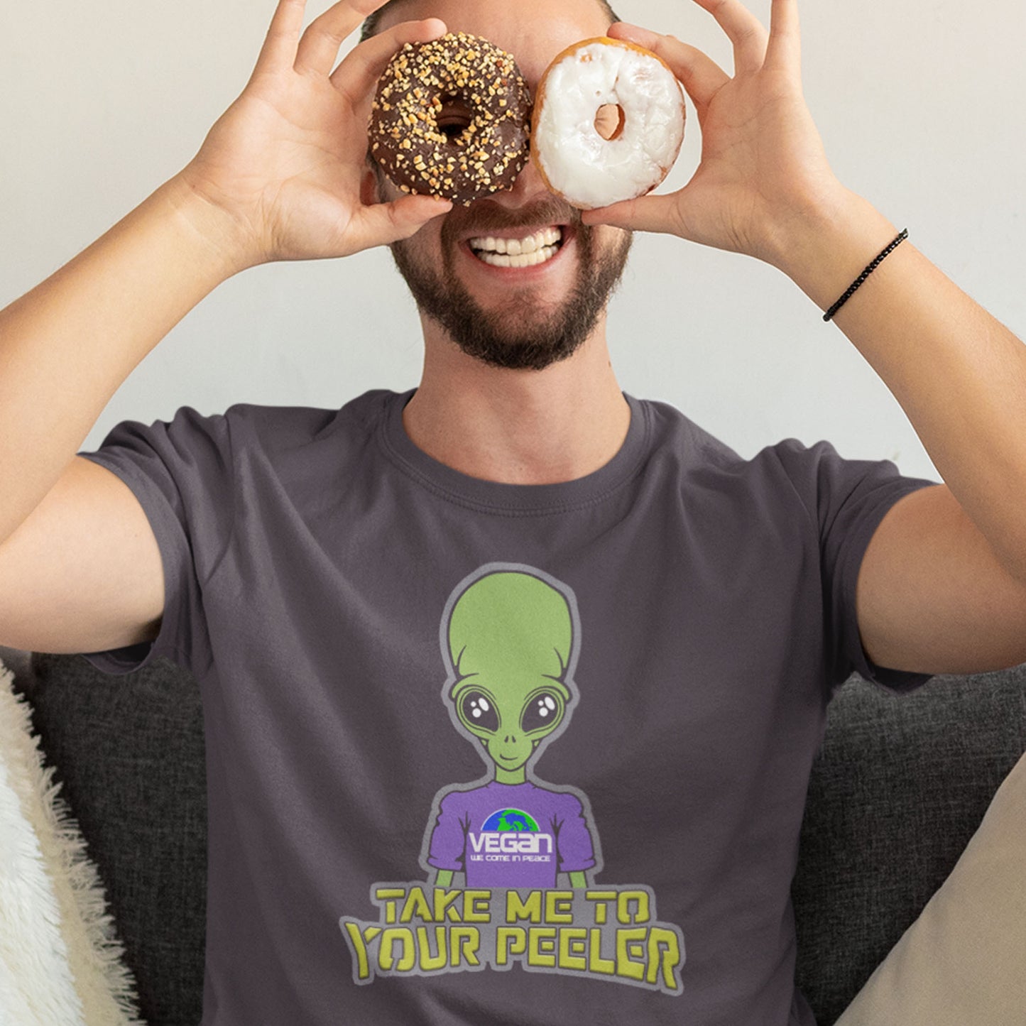 Person wearing a t-shirt with an alien graphic and text, holding donuts over their eyes. A plant based t-shirt design for anyone that thinks aliens must be vegans, otherwise they would have been farming us years ago. This unique alien design is for all those conspiracy theorists out there. Made from 100% organic ring-spun cotton, this vegan t-shirt is unisex, high-quality, super comfy, and best of all, eco-friendly.