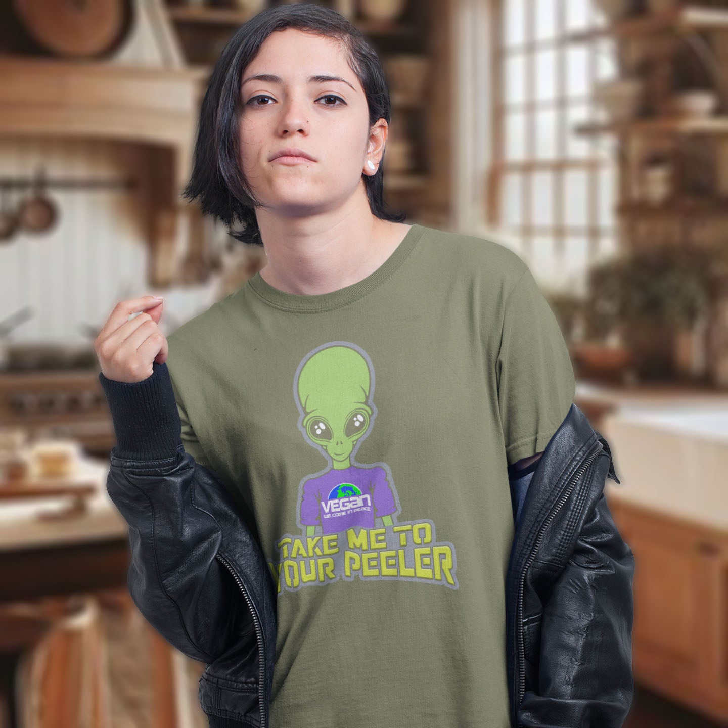 Person wearing a khaki t-shirt with an alien graphic and text in a kitchen setting. A plant based t-shirt design for anyone that thinks aliens must be vegans, otherwise they would have been farming us years ago. This unique alien design is for all those conspiracy theorists out there. Made from 100% organic ring-spun cotton, this vegan t-shirt is unisex, high-quality, super comfy, and best of all, eco-friendly.
