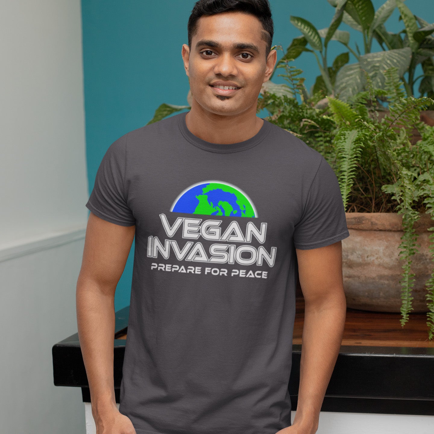 Man wearing a 'Vegan Invasion' t-shirt with plants in the background. This vegan meat free t shirt design plays on the idea that other people view vegans as alien. Reassure people that you are a peaceful creature and remind them that you help to save the planet. Made from 100% organic ring-spun cotton, this plant based meat free t shirt is unisex, high-quality, super comfy, and best of all, eco-friendly.