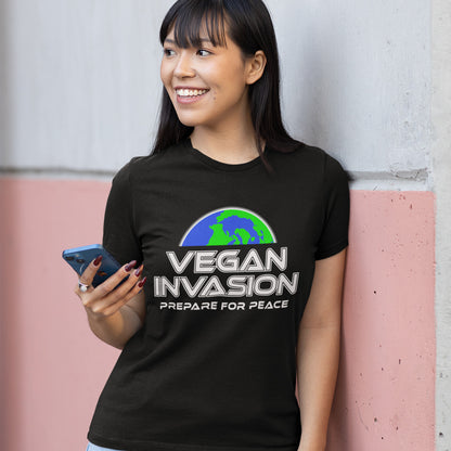 Person wearing a black t-shirt with 'Vegan Invasion: Prepare for Peace' text and graphic, holding a phone. This vegan meat free t shirt design plays on the idea that other people view vegans as alien. Reassure people that you are a peaceful creature and remind them that you help to save the planet. Made from 100% organic ring-spun cotton, this plant based meat free t shirt is unisex, high-quality, super comfy, and best of all, eco-friendly.