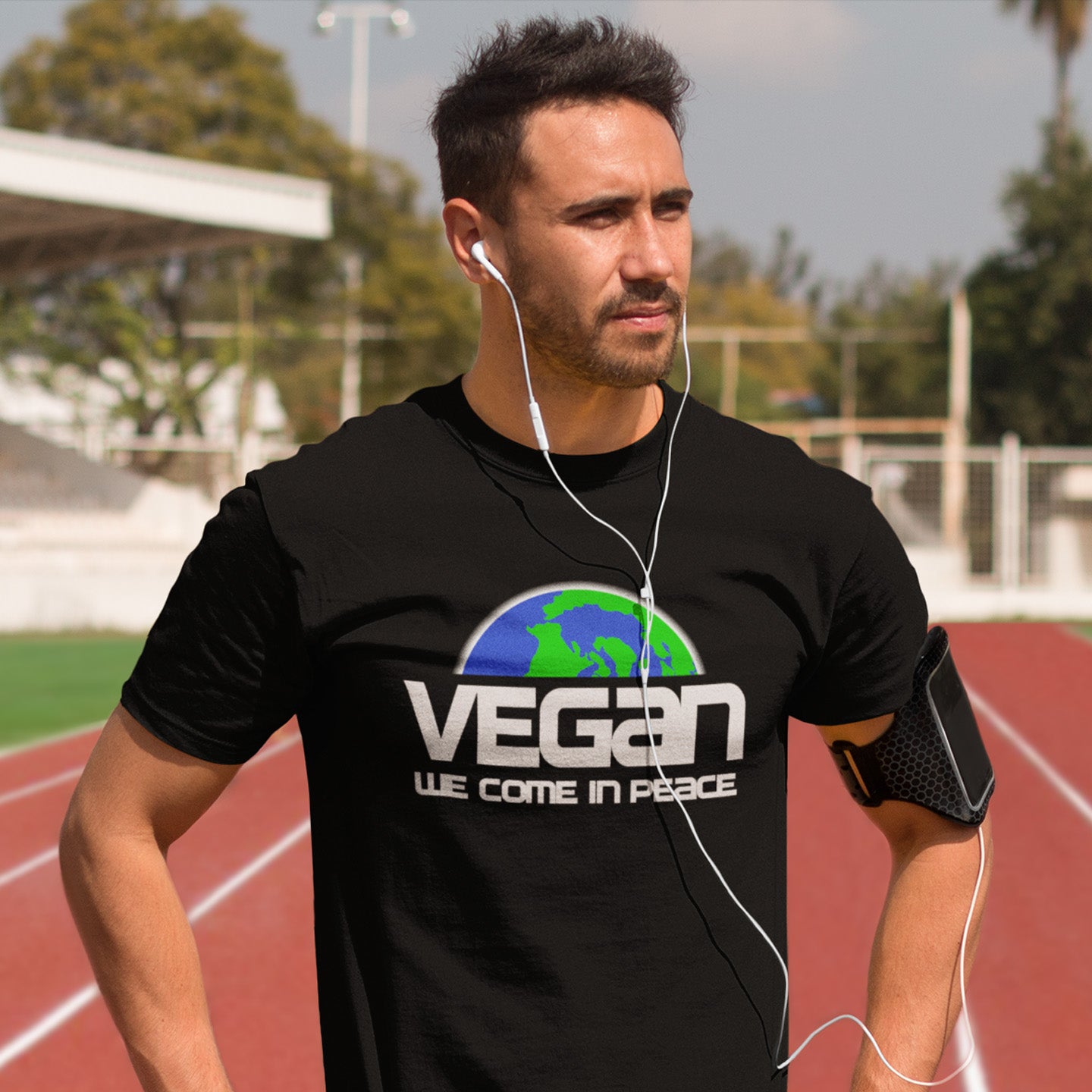 Man wearing a black t-shirt with 'Vegan We Come In Peace' on a track field.  This vegan dairy free t shirt design is for any vegan who feels like they are seen as an alien by others. Reassure people that you are a peaceful creature and want to save the planet. Made from 100% organic ring-spun cotton, this plant based meat free t shirt is unisex, high-quality, super comfy, and best of all, eco-friendly.