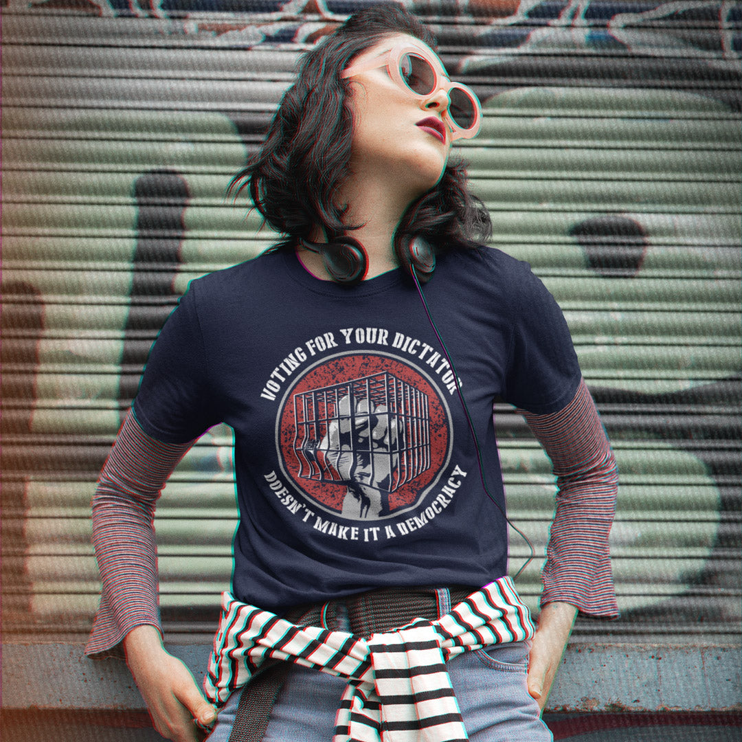 A woman wearing a navy graphic t-shirt with a circular red and black print, layered over a striped long-sleeve shirt and jeans, posing in front of a graffiti-covered metal shutter.