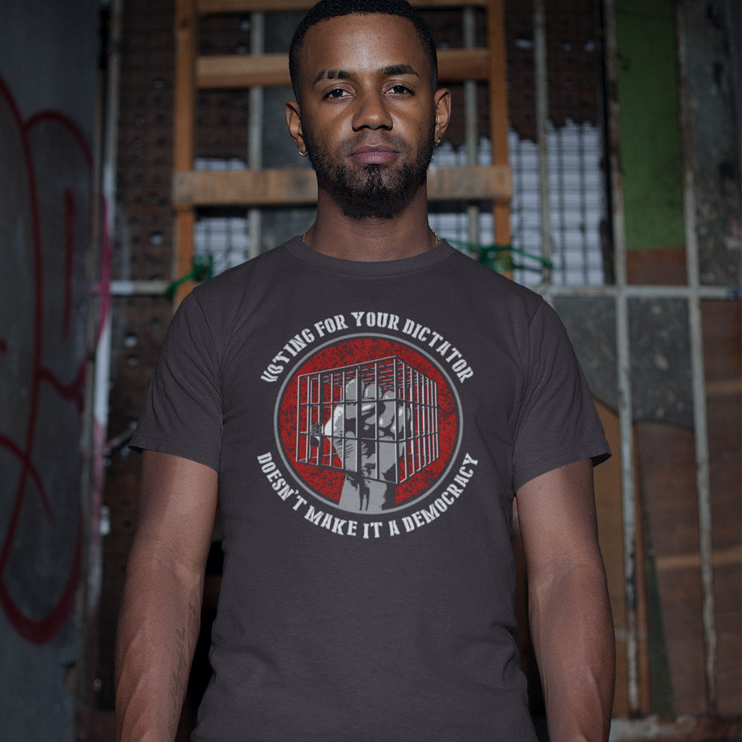 A man wearing a dark gray graphic t-shirt with a red and white circular design featuring a portrait and text, set against a gritty urban alley background.