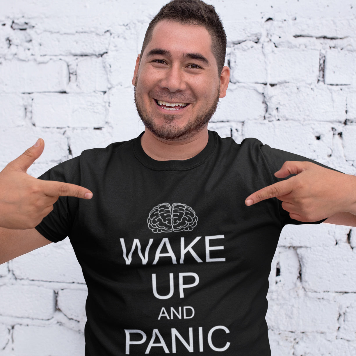 Man wearing a black t-shirt with 'Wake Up and Panic' text and pointing at it, white brick wall background. This satirical 'stay calm' anti-establishment t-shirt suggests we have been calm too long and need of waking up and panic. Keeping calm got us into this mess, it's time to wake up. 100% organic ring-spun cotton, this anti-government t-shirt is unisex, high-quality, super comfy, and best of all, eco-friendly.