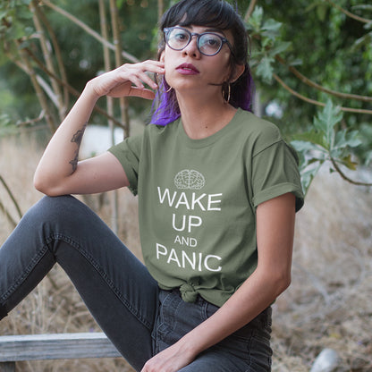 Person wearing a khaki t-shirt with 'Wake Up and Panic' text, sitting outdoors. This satirical 'stay calm' anti-establishment t-shirt suggests we have been calm too long and need of waking up and panic. Keeping calm got us into this mess, it's time to wake up. 100% organic ring-spun cotton, this anti-government t-shirt is unisex, high-quality, super comfy, and best of all, eco-friendly.