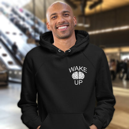 Man wearing a black hoodie with 'Wake Up' text and brain graphic in an indoor setting. This satirical 'stay calm' anti establishment hoodie suggests we have been calm too long and need of waking up and panic. Keeping calm got us into this mess, it's time to wake up. Comfortable and practical. It's extra soft and has a convenient front pouch pocket. Made from organic cotton and recycled polyester, this activist hoodie is a great eco-friendly choice.
