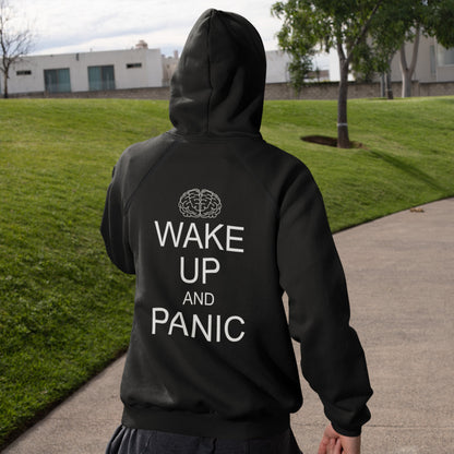 Person wearing a black hoodie with 'Wake Up and Panic' text on the back, walking outdoors. This satirical 'stay calm' rebellion hoodie suggests we have been calm too long and need of waking up and panic. Keeping calm got us into this mess, it's time to wake up. Comfortable and practical. It's extra soft and has a convenient front pouch pocket. Made from organic cotton and recycled polyester, this activist hoodie is a great eco-friendly choice.