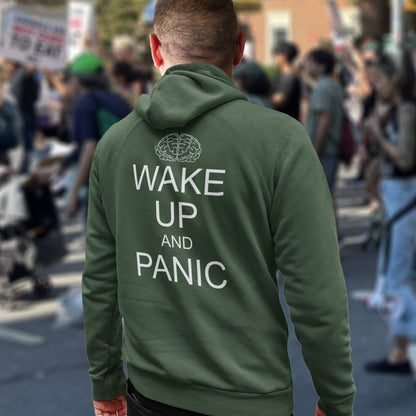 Person wearing a bottle  green hoodie with 'Wake Up and Panic' text at a protest rally. This satirical 'stay calm' rebellion hoodie suggests we have been calm too long and need of waking up and panic. Keeping calm got us into this mess, it's time to wake up. Comfortable and practical. It's extra soft and has a convenient front pouch pocket. Made from organic cotton and recycled polyester, this activist hoodie is a great eco-friendly choice.