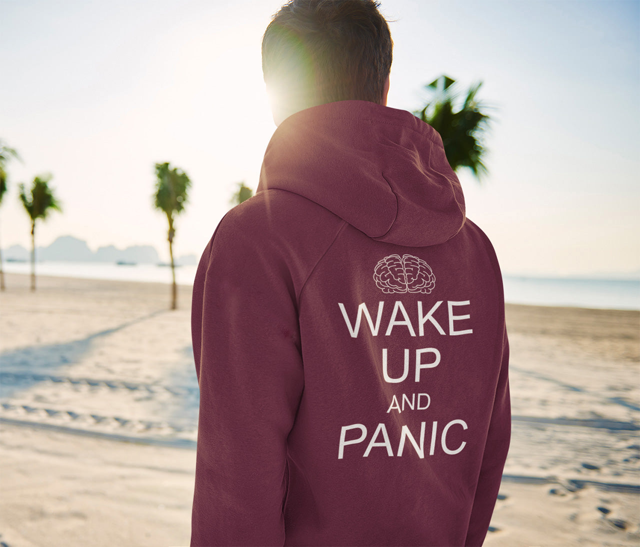 Person wearing a burgundy hoodie with 'Wake Up and Panic' text on the beach. This satirical 'stay calm' rebellion hoodie suggests we have been calm too long and need of waking up and panic. Keeping calm got us into this mess, it's time to wake up. Comfortable and practical. It's extra soft and has a convenient front pouch pocket. Made from organic cotton and recycled polyester, this activist hoodie is a great eco-friendly choice.