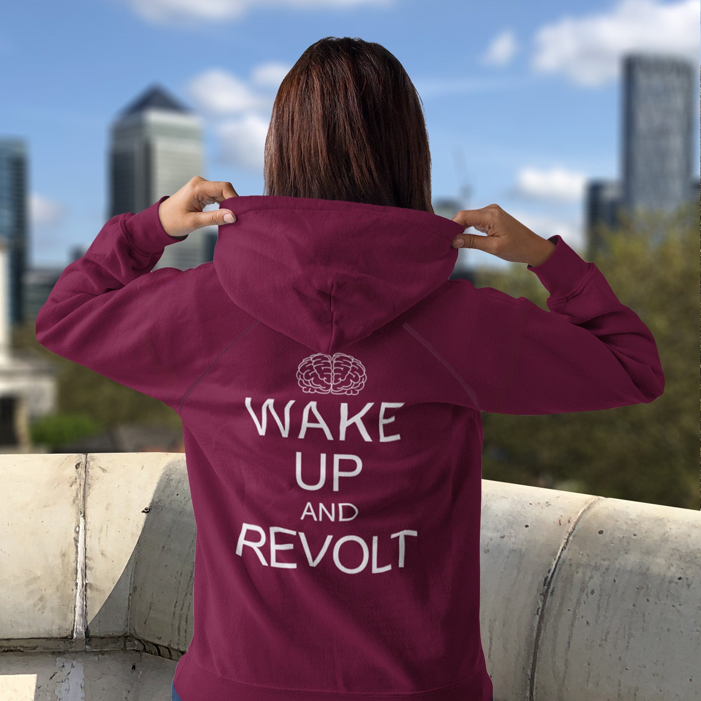 Person wearing a burgundy hoodie with 'Wake Up and Revolt' text, standing on a rooftop with cityscape in the background. This satirical 'stay calm' hoodie suggests we have been calm too long and need of waking up and fighting for our right instead. Keeping calm got us into this mess, it's time to wake up. Comfortable and practical. It's extra soft and has a convenient front pouch pocket. Made from organic cotton and recycled polyester, this anti-establishment hoodie is a great eco-friendly choice.