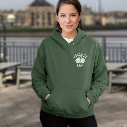 Person wearing a bottle green hoodie with 'Wake Up' text, standing outdoors. This satirical 'stay calm' hoodie suggests we have been calm too long and need of waking up and fighting for our right instead. Keeping calm got us into this mess, it's time to wake up. Comfortable and practical. It's extra soft and has a convenient front pouch pocket. Made from organic cotton and recycled polyester, this anti-establishment hoodie is a great eco-friendly choice.