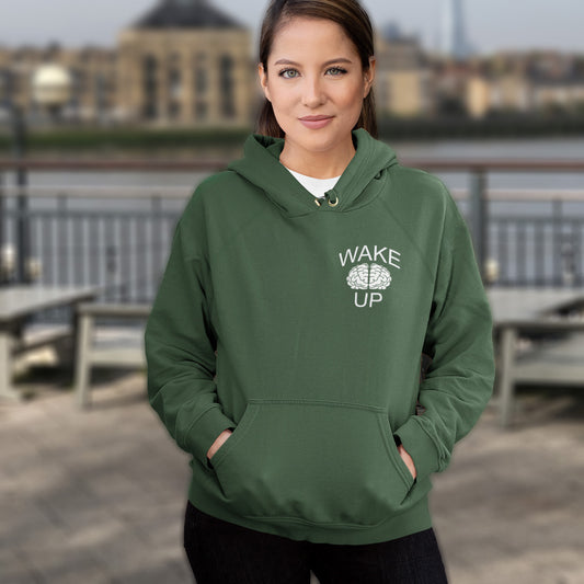 Person wearing a bottle green hoodie with 'Wake Up' text, standing outdoors. This satirical 'stay calm' hoodie suggests we have been calm too long and need of waking up and fighting for our right instead. Keeping calm got us into this mess, it's time to wake up. Comfortable and practical. It's extra soft and has a convenient front pouch pocket. Made from organic cotton and recycled polyester, this anti-establishment hoodie is a great eco-friendly choice.