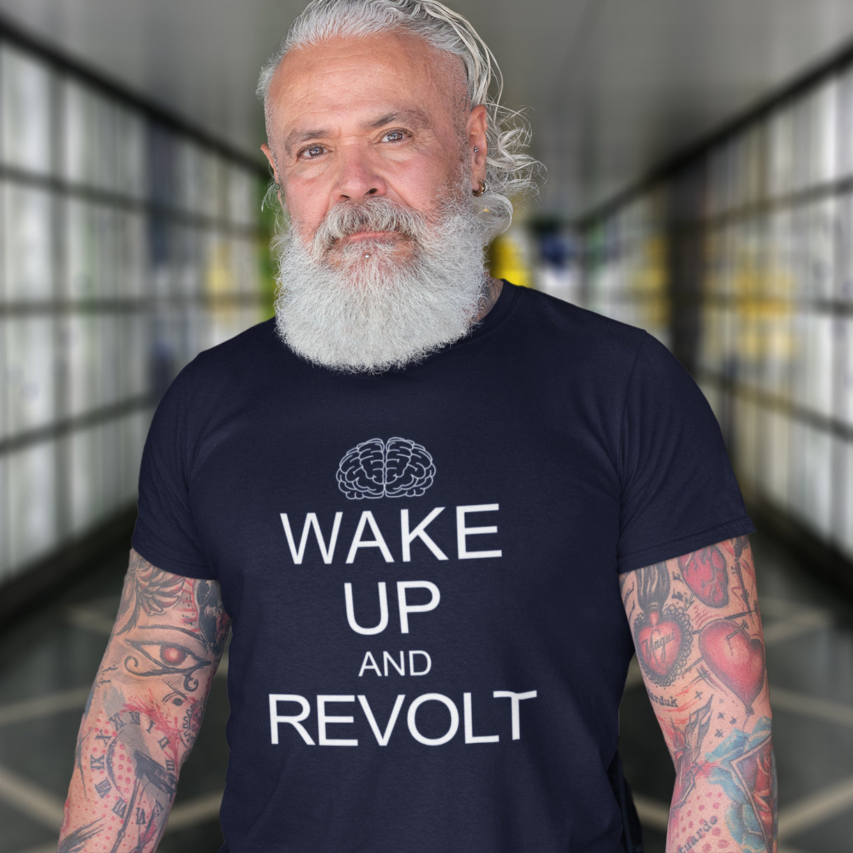 Man wearing a French navy t-shirt with 'Wake Up and Revolt' text in a blurred indoor setting. This satirical 'stay calm' t-shirt suggests we have been calm too long and need of waking up and fighting for our right instead. Keeping calm got us into this mess, it's time to wake up. Made from 100% organic ring-spun cotton, this counterculture t-shirt is unisex, high-quality, super comfy, and best of all, eco-friendly.