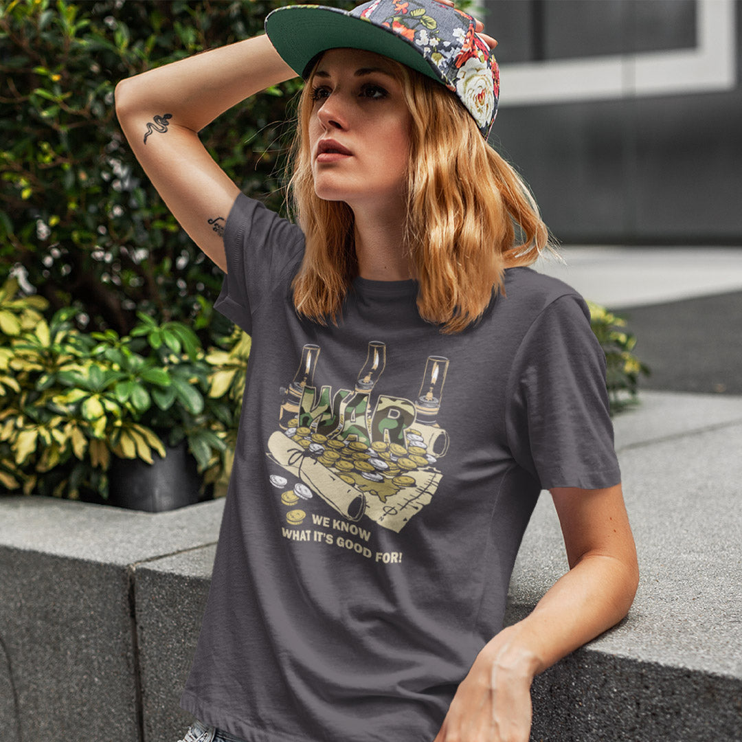 A woman wearing a dark gray graphic t-shirt and a green floral baseball cap, leaning against a concrete wall in an outdoor urban setting.
