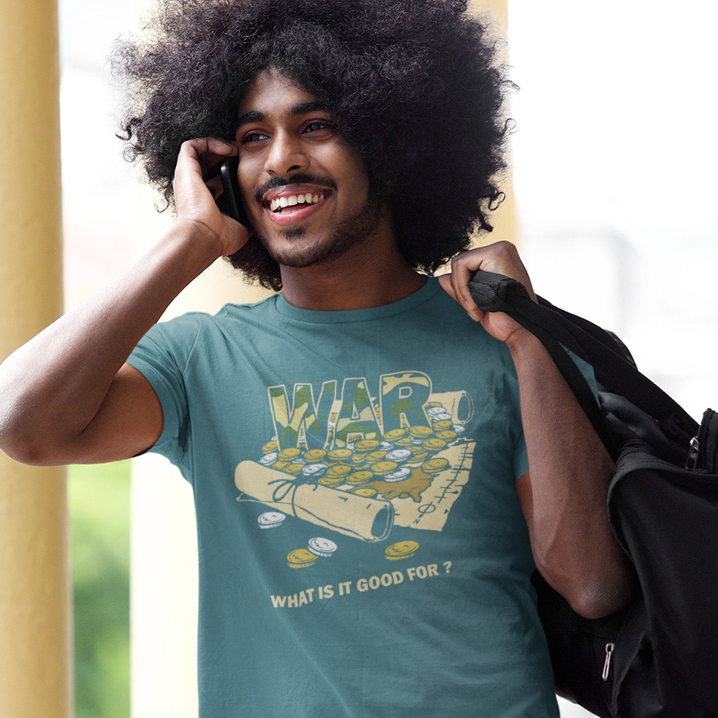 Man wearing a teal t-shirt with a graphic design, holding a phone to his ear and a black bag. A satirical anti-war t-shirt suggesting we know what it's good for, money and land deeds for starters. Expose the big business of War with this unique design made for any anti-war demonstration. Made from 100% organic ring-spun cotton, this political t-shirt is unisex, high-quality, super comfy, and best of all, eco-friendly.