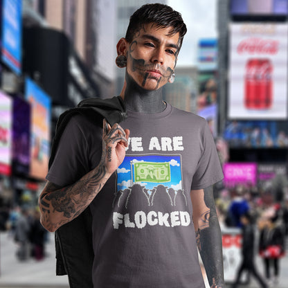 Tattooed man standing in Time square wearing a "we are flocked" t shirt, A funny broken society t shirt depicting people as a flock of sheep obsessed with money and screens. This urban art design uses Satirical humour to address the direction of our society, and the main forces of attraction in it. Made from 100% organic ring-spun cotton, these social issues t shirts are unisex, high quality, super comfy, and best of all, eco-friendly.