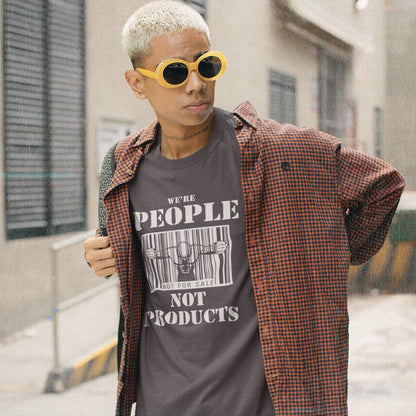 Man standing outside, wearing an anthracite grey t-shirt with "WE'RE PEOPLE NOT PRODUCTS" design.