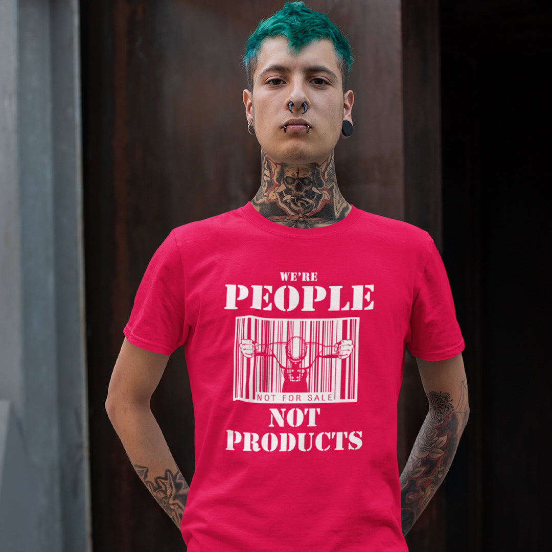 Man standing with his hands behind his back, wearing a red t-shirt with "WE'RE PEOPLE NOT PRODUCTS" design.