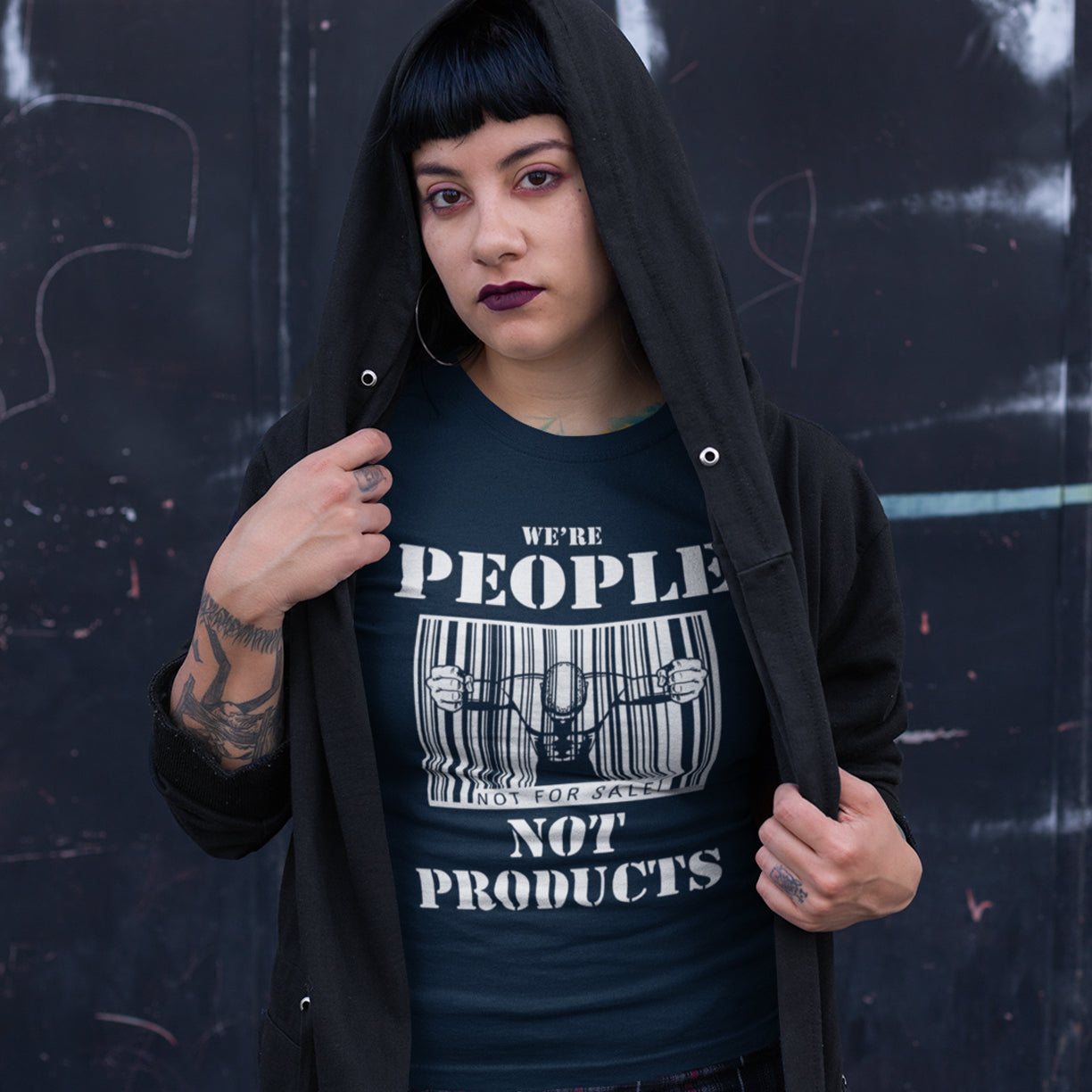 Woman wearing a French navy blue t shirt with 'we're people not products' text. An anti capitalism t shirt highlighting the dehumanisation of people in a money obsessed society. A fantastic choice for any anti capitalism protest or to just create social awareness. Made from 100% organic ring-spun cotton, this anti consumerism t shit is unisex, high-quality, super comfy, and best of all, eco-friendly.