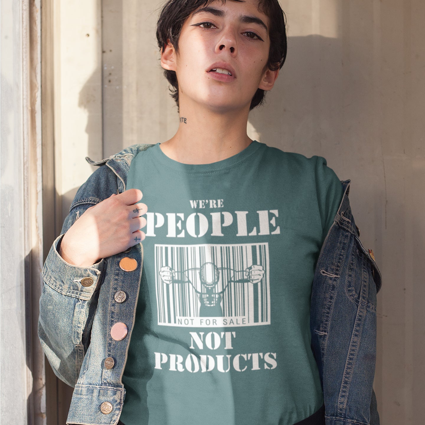 Person stood in a doorway wearing a 'we're people not products' t shirt. An anti capitalism t shirt highlighting the dehumanisation of people in a money obsessed society. A fantastic choice for any anti capitalism protest or to just create social awareness. Made from 100% organic ring-spun cotton, this anti consumerism t shit is unisex, high-quality, super comfy, and best of all, eco-friendly.