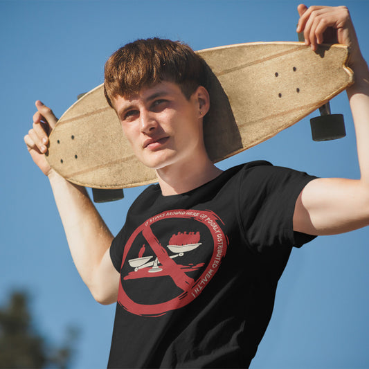 A young man outdoors under a clear blue sky holds a skateboard over his shoulders while wearing a black t-shirt with a red and white graphic on the chest.
