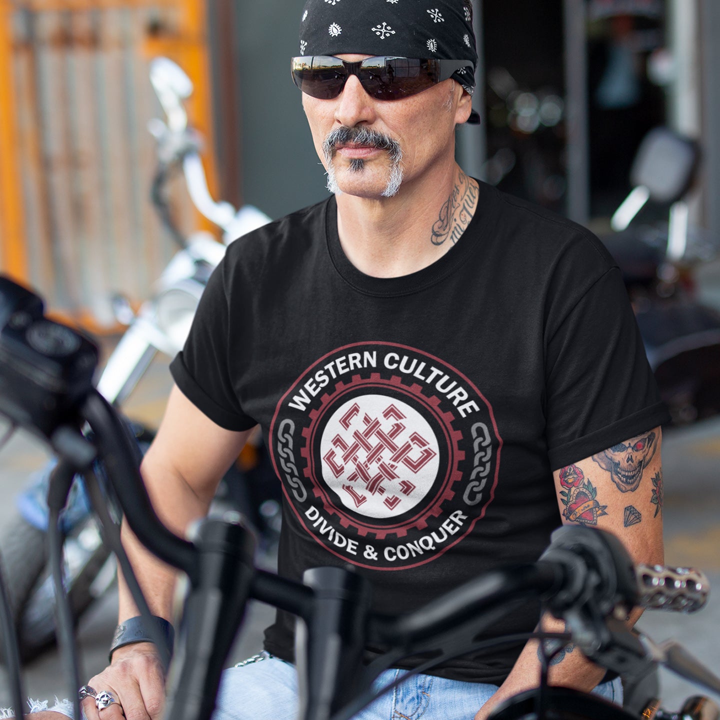 Man wearing a black t-shirt with 'Western Culture Divide & Conquer' design, sitting on a motorcycle. This counter culture t shirt questions the politics of western society. Let's drop the façade that western culture is more civilised and advanced. This design highlights a method of people management that has worked for the Western elite for centuries. Made from 100% organic ring-spun cotton, this broken society t shirt is unisex, high-quality, super comfy, and best of all, eco-friendly.
