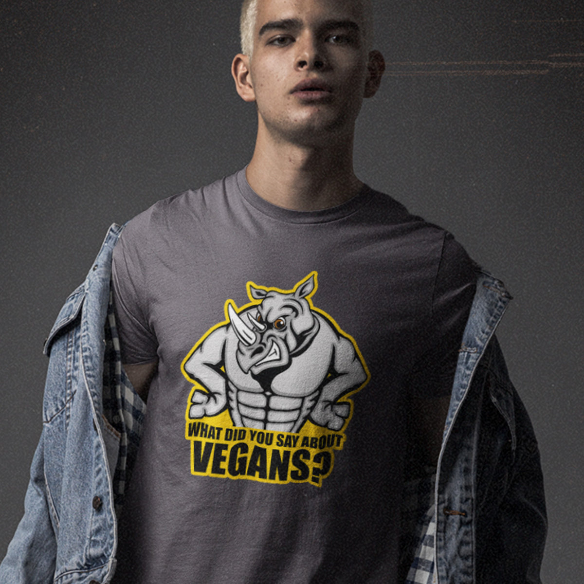 A man standing against a grey wall, wearing an anthracite grey crew neck t-shirt with a cartoon Rhino design and the caption "WHAT DID YOU SAY ABOUT VEGANS?".