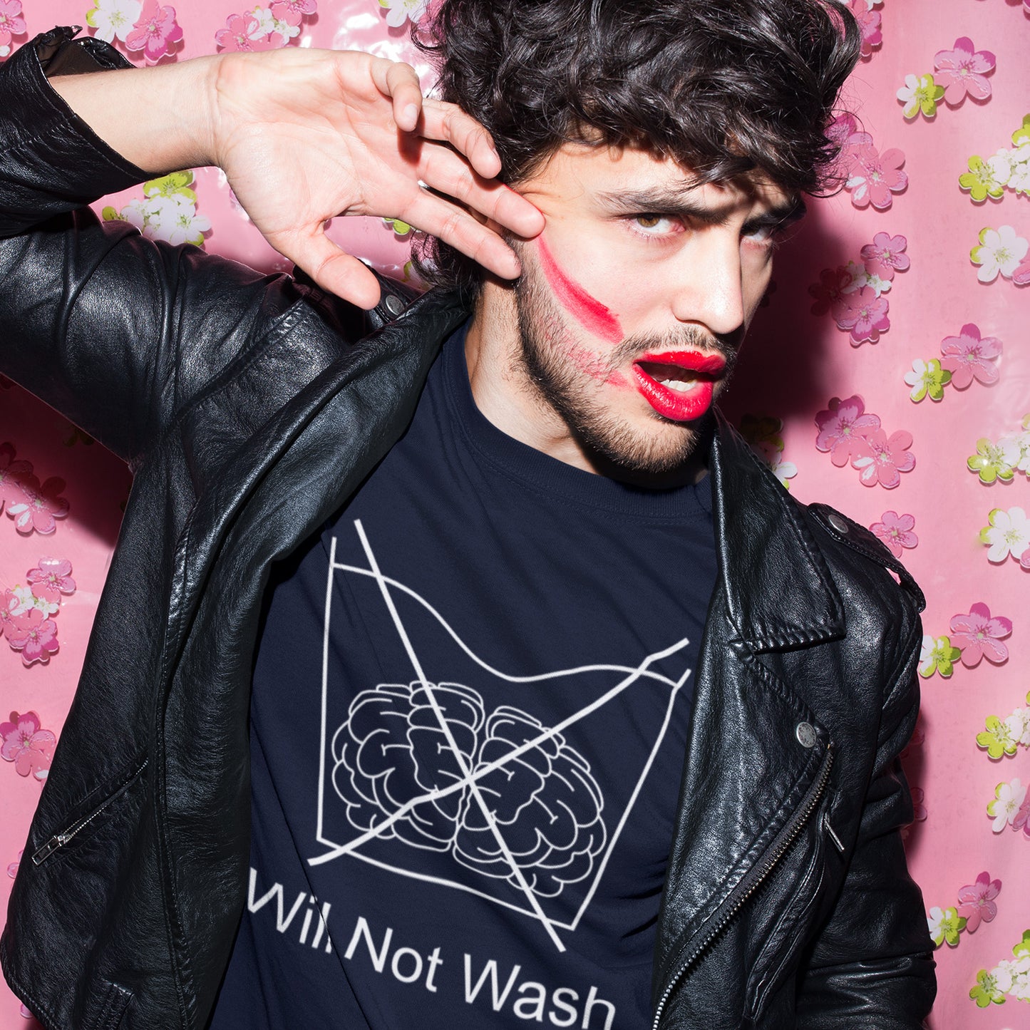 Man wearing a black leather jacket and a black t-shirt with a graphic design, posing against a pink floral background. A self worth t shirt promoting a strong mind and a resistance to brainwashing. this unique anti-establishment t-shirt design is a play on washing instructions and highlights the mass influence and indoctrination in modern society. Made from 100% organic ring-spun cotton, this clever slogan t shirt is unisex, high-quality, super comfy, and best of all, eco-friendly.