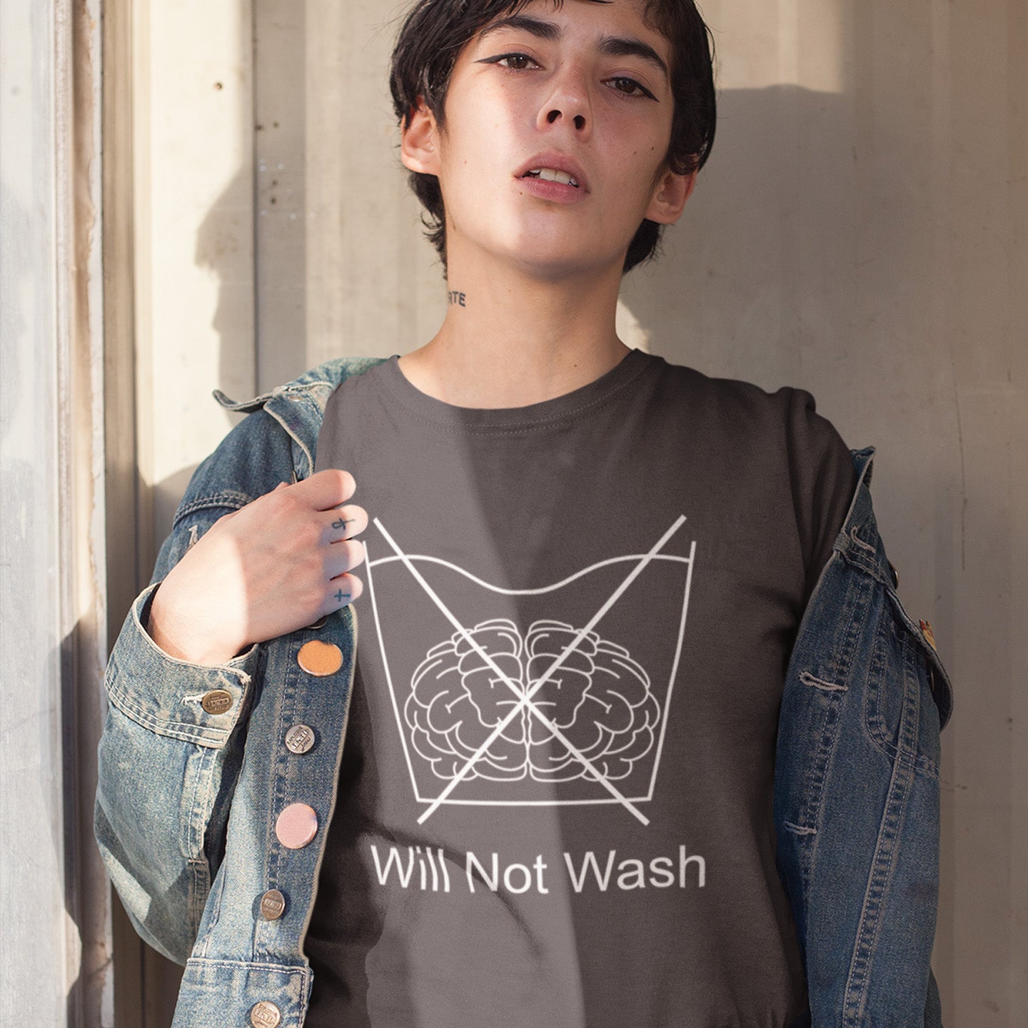 Person wearing an anthracite t-shirt with a graphic design and text, standing against a neutral wall. A self worth t shirt promoting a strong mind and a resistance to brainwashing. this unique anti-establishment t-shirt design is a play on washing instructions and highlights the mass influence and indoctrination in modern society. Made from 100% organic ring-spun cotton, this clever slogan t shirt is unisex, high-quality, super comfy, and best of all, eco-friendly.