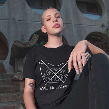 Person wearing a black t-shirt with a graphic design and text, sitting against a textured wall. A self worth t shirt promoting a strong mind and a resistance to brainwashing. this unique anti-establishment t-shirt design is a play on washing instructions and highlights the mass influence and indoctrination in modern society. Made from 100% organic ring-spun cotton, this clever slogan t shirt is unisex, high-quality, super comfy, and best of all, eco-friendly.