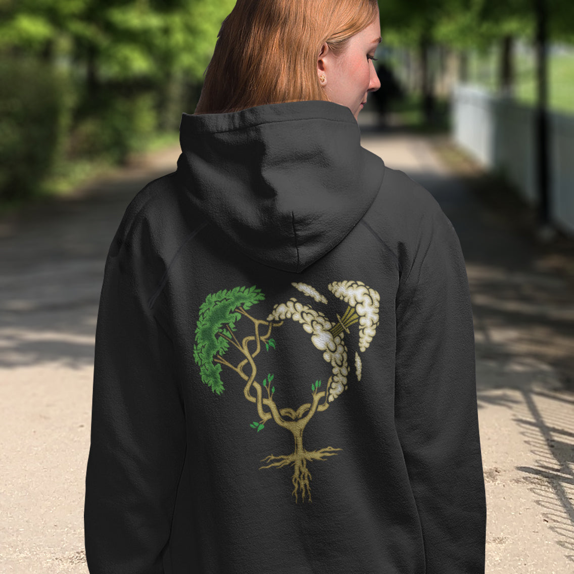 Person wearing a black hoodie with a tree and flower design on the back, standing outdoors. A women's rights hoodie design that pays homage to women and promotes social awareness of how most destructive elements of humankind come from men. Women create life, men destroy it. Comfortable and practical. It's extra soft and has a convenient front pouch pocket. Made from organic cotton and recycled polyester, this women's rights hoodie is a great eco-friendly choice.