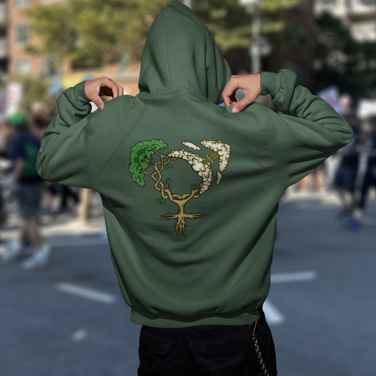Person wearing a bottle green hoodie with a tree design on the back, standing in an urban setting. A women's rights hoodie design that pays homage to women and promotes social awareness of how most destructive elements of humankind come from men. Women create life, men destroy it. Comfortable and practical. It's extra soft and has a convenient front pouch pocket. Made from organic cotton and recycled polyester, this women's rights hoodie is a great eco-friendly choice.