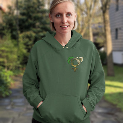 Woman wearing a bottle green hoodie with a decorative emblem outdoors. A women's rights hoodie design that pays homage to women and promotes social awareness of how most destructive elements of humankind come from men. Women create life, men destroy it. Comfortable and practical. It's extra soft and has a convenient front pouch pocket. Made from organic cotton and recycled polyester, this women's rights hoodie is a great eco-friendly choice.