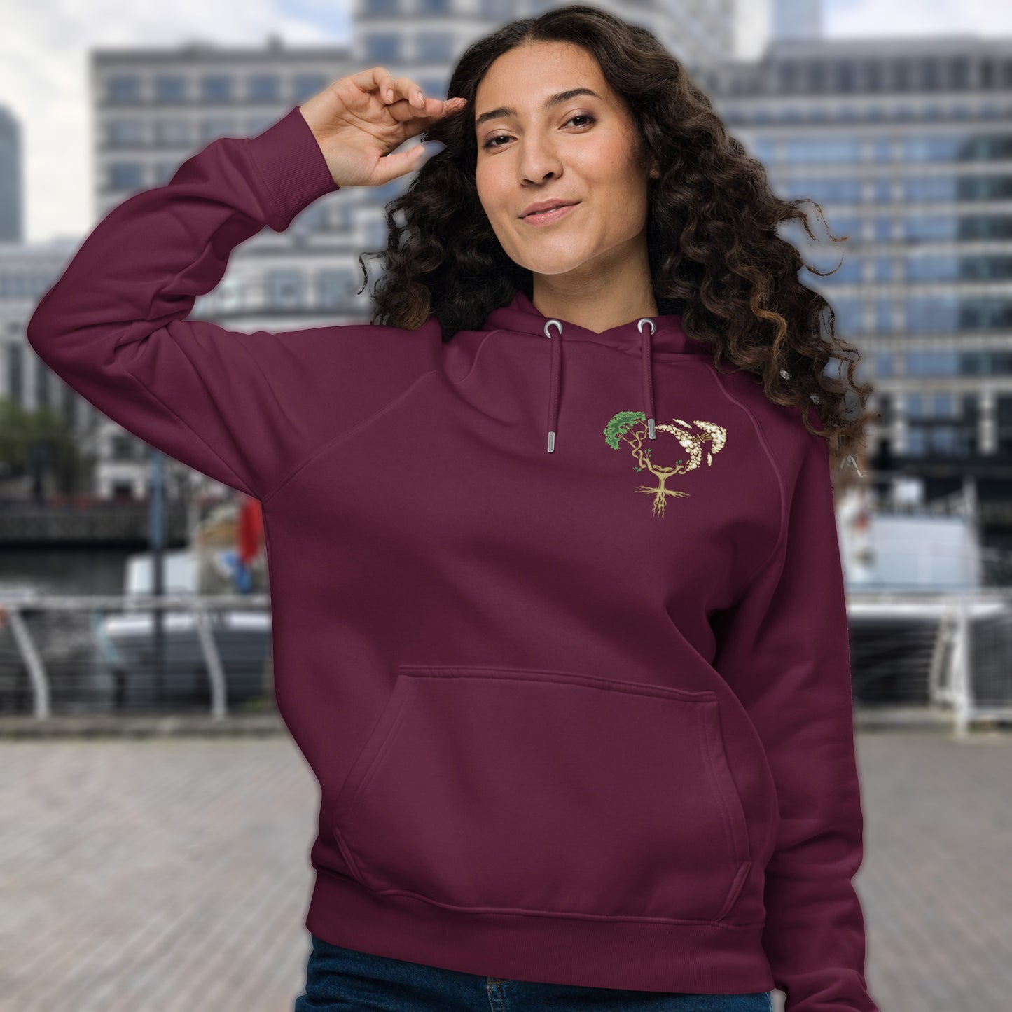 Woman wearing a burgundy hoodie with a design in an urban setting. A women's rights hoodie design that pays homage to women and promotes social awareness of how most destructive elements of humankind come from men. Women create life, men destroy it. Comfortable and practical. It's extra soft and has a convenient front pouch pocket. Made from organic cotton and recycled polyester, this women's rights hoodie is a great eco-friendly choice.