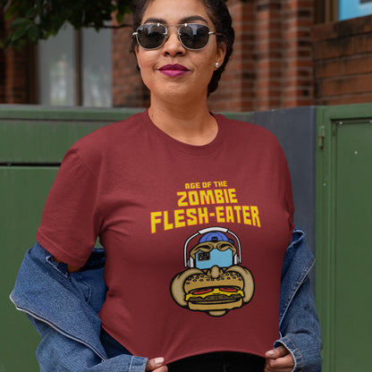 A woman wearing a burgundy graphic t-shirt with yellow text reading 'AGE OF THE ZOMBIE FLESH-EATER' and a cartoon zombie burger graphic, styled with a blue denim jacket off her shoulders.