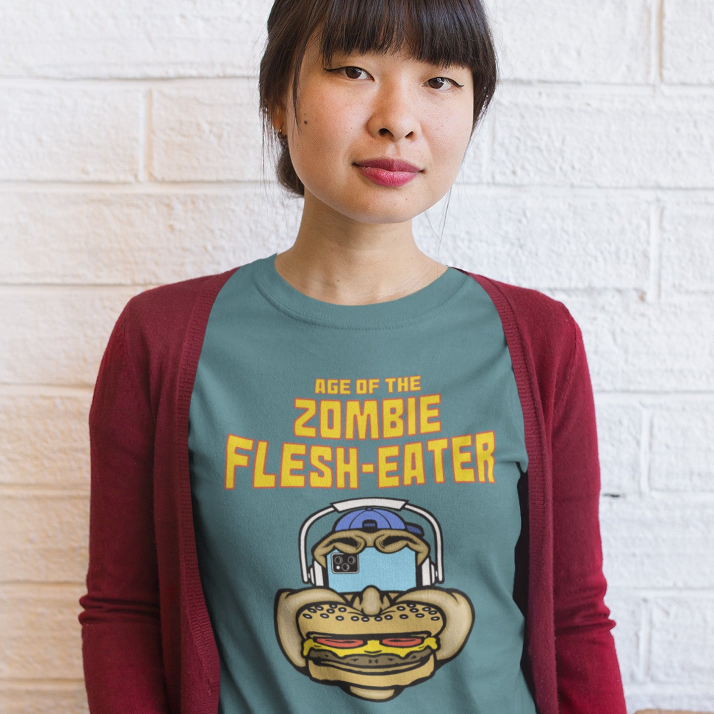 Person wearing a t-shirt with a zombie graphic and text against a white brick wall. This meat free t-shirt design plays on the interpretation of a late 70's B rate movie. As a modern day vegan surrounded by people hypnotised on their mobile phone while eating meat based fast food, you may be forgiven for thinking you are living in the age of the zombie flesh-eater. Made from 100% organic ring-spun cotton, this meat free t shirt design is unisex, high-quality, super comfy, and best of all, eco-friendly.